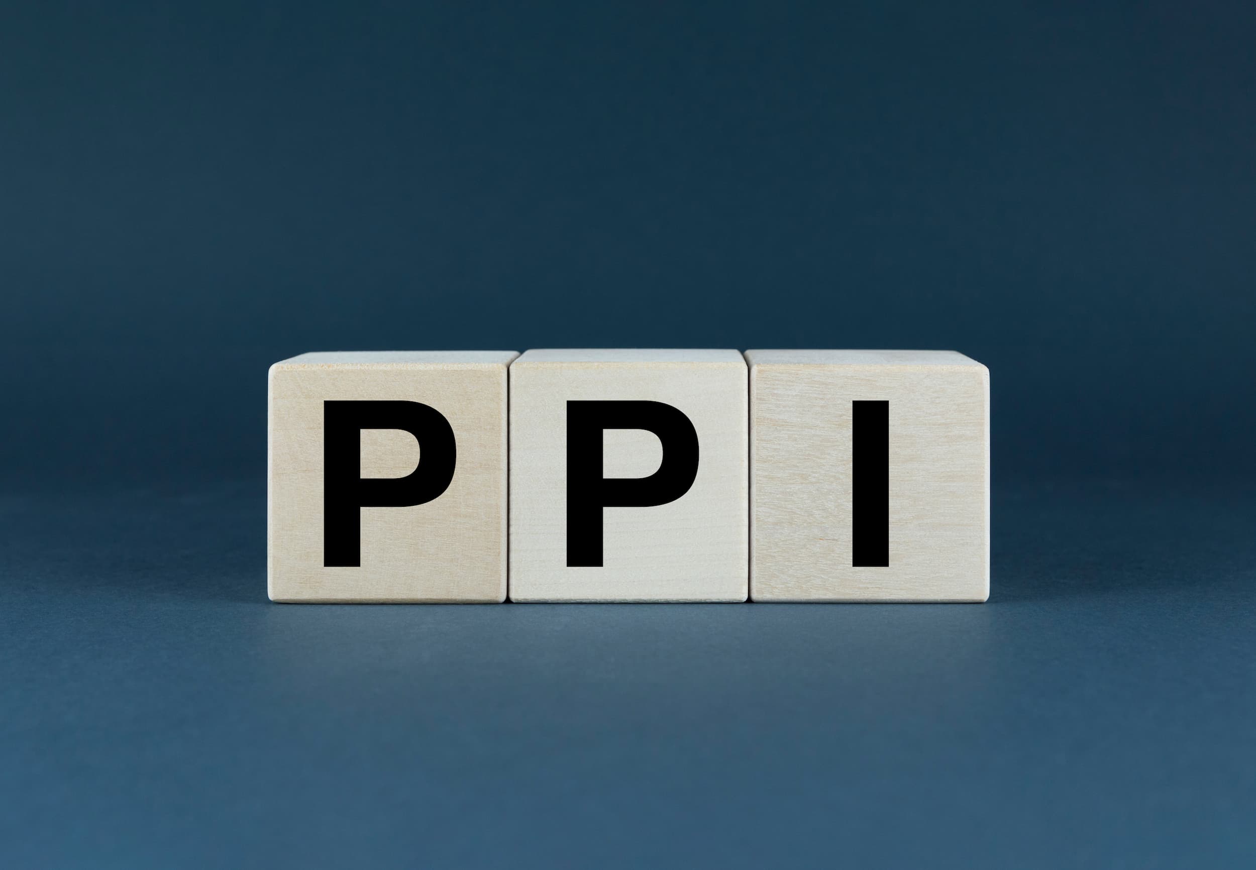 Three wooden cubes on a navy blue background, each emblazoned with a letter to spell ‘PPI’.