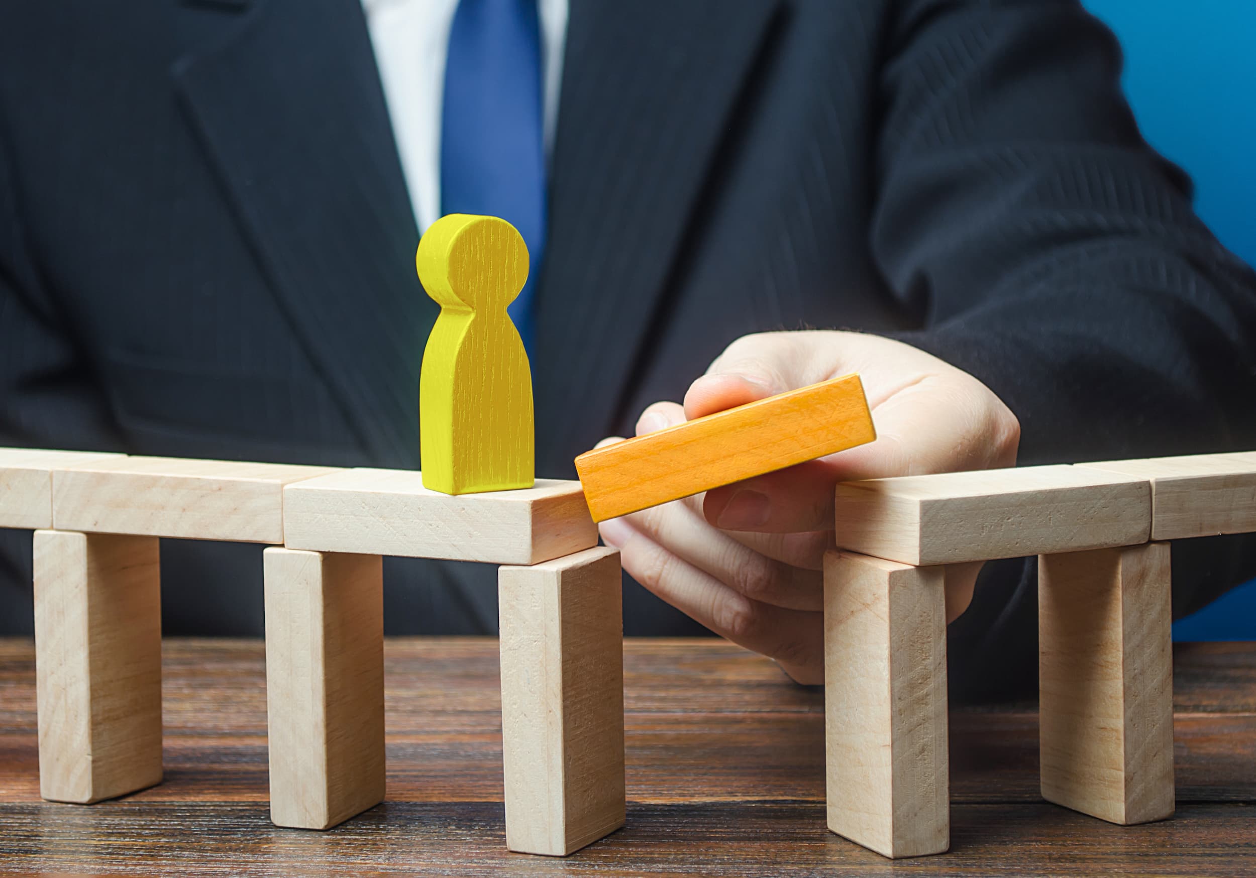 A man adds the final block to complete a bridge made out of blocks, representing bridging finance.